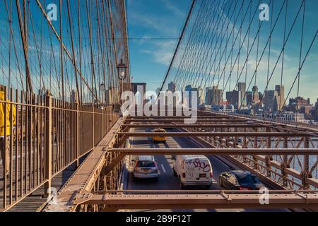 Ponte di Brooklyn con vista diurna a New York con auto in movimento il ponte, lo skyline e le nuvole nel cielo sullo sfondo Foto Stock