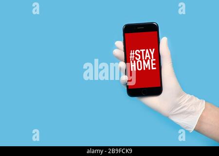 Una mano in un guanto tiene un telefono con le parole rimanere a casa isolata. Quarantena Foto Stock
