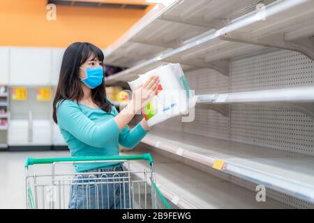 Donna asiatica che guarda Supermarket vuoto carta igienica scaffali in mezzo COVID-19 Coronavirus paure, acquirenti panico acquisto e stoccaggio carta igienica preparazione Foto Stock