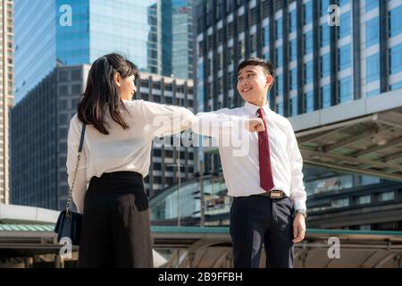 Gomito bump è nuovo saluto per evitare la diffusione di coronavirus. Due amici d'affari asiatici si incontrano di fronte all'edificio degli uffici. Invece di salutare Foto Stock