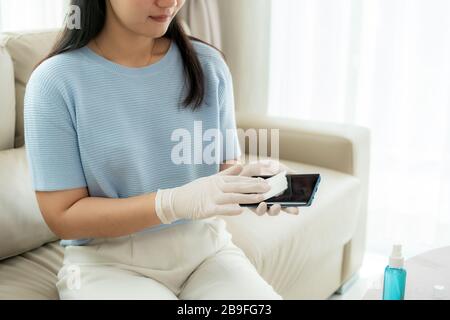 La donna asiatica spruzza alcol, disinfettante spray sul telefono cellulare, prevenire l'infezione del virus Covid-19, la contaminazione di germi o batteri, strofinare o c Foto Stock
