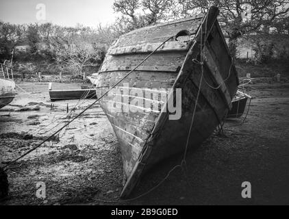 'Su il Creek senza una pagaia'. Nero e bianco di scafo di legno invecchiato sul suo lato con bassa marea. Decadendo via e non si prende cura di. Meravigliose texture di legno Foto Stock