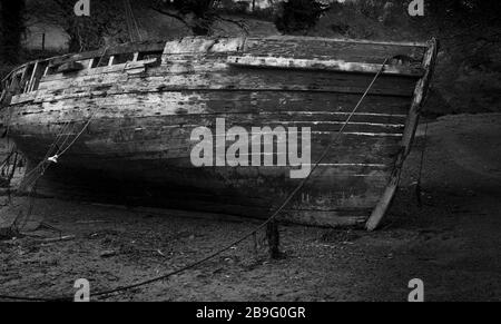 'Su il Creek senza una pagaia'. Nero e bianco di scafo di legno invecchiato sul suo lato con bassa marea. Decadendo via e non si prende cura di. Meravigliose texture di legno Foto Stock