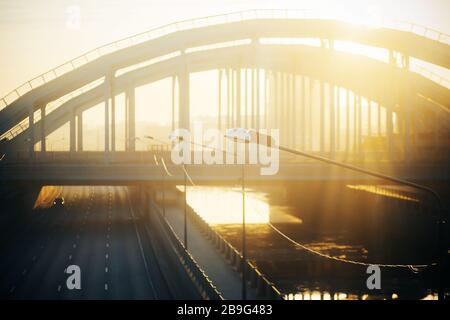 Un'immagine sfocata di un ponte metallico curvo su un fiume, attraverso il quale passano i raggi del sole. Foto Stock