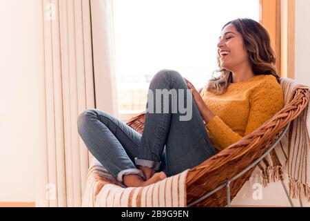 Donna ottimista seduta in una comoda sedia in rattan a casa Foto Stock