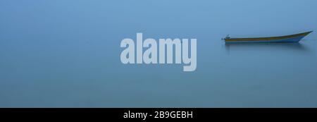 Sole barca al mattino presto in acque blu e nebbia in lontananza senza linea di orizzonte banda mare in Ohoidertawun spiaggia, Maluku, Indonesia Foto Stock