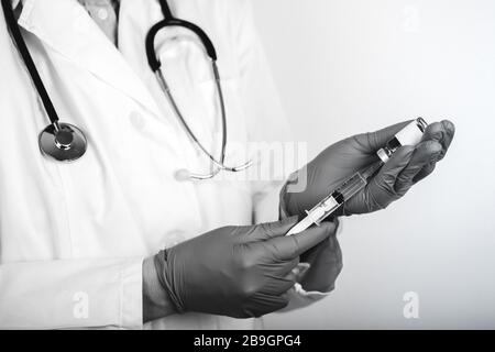 Medico in camice bianco da laboratorio su fondo bianco contenente una siringa con un medicinale in mano, un'iniezione. Foto in bianco e nero. Foto Stock