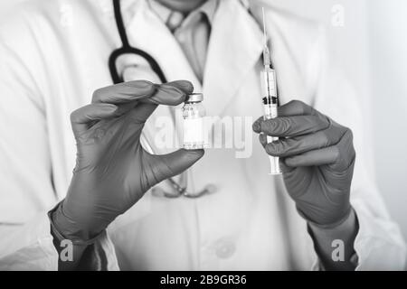 Medico in camice bianco da laboratorio e guanti sterili contenenti siringa e medicinale in fiala. Foto in bianco e nero. Foto Stock