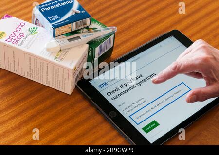 Una donna che utilizza un ipad per controllare il sito web NHS per consigli sui simpton Coronavirus Covid-19. Con medicinali e termometro. Foto Stock