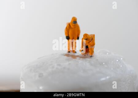 Immagine concettuale per Coronavirus con persone in miniatura su una barra di sapone in tute di nocciola test per la ricerca di batteri. Foto Stock