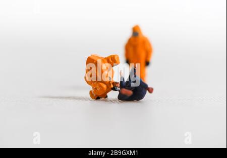 Un'immagine concettuale per Coronavirus di persone in miniatura in abiti Hazmat tendenti ad un uomo malato. Foto Stock