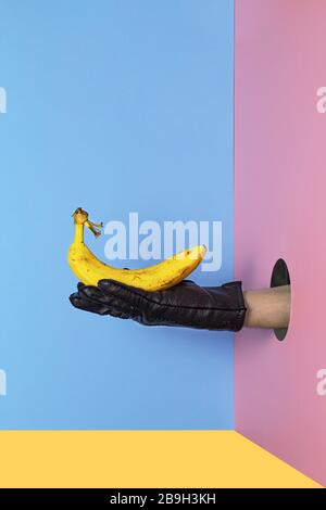 Mano tenendo giallo Banana su uno sfondo colorato con spazio copia. Composizione trendy minima. Banana in mano di un uomo Foto Stock