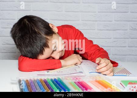 Sconvolto scolaro noioso facendo i compiti. Concetto di istruzione, scuola, difficoltà di apprendimento. Bambino stanco di fare i compiti studiando con la penna addormentata su OPE Foto Stock