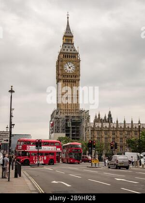 Big ben sotto impalcatura. Vista sulla strada dell'iconico monumento di Londra in fase di ristrutturazione, mentre gli autobus rossi passano in primo piano. Foto Stock