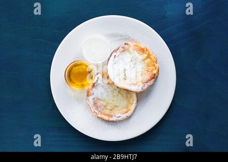 Frittelle di formaggio casolare o frittelle con miele su sfondo di legno blu Foto Stock