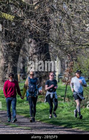 Clapham Common, Londra, Regno Unito. 24 Marzo 2020. Joggers mescolare con gli escursionisti - la gente esce sul Clapham comune per ottenere i loro giorni di esercizio in - la maggior parte pratica sociale a distanza, ma è quasi occupato come un normale giorno di primavera. Il primo giorno dell'epidemia di "blocco" a Clapham - Anti Coronavirus (Covid 19) a Londra. Credit: Guy Bell/Alamy Live News Foto Stock