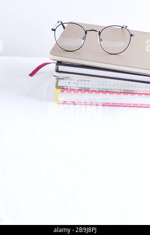 Raccolta di diversi libri di appunti colorati per note e annotazioni con occhiali sulla parte superiore di un tavolo bianco contro una parete grigio chiaro, spazio per le copie. Wo Foto Stock