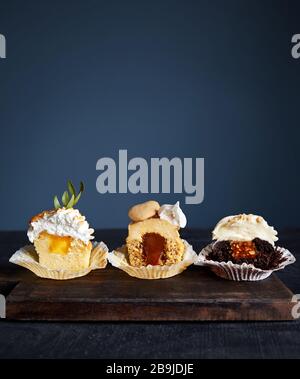 Taglio di cupcake assortiti con roba diversa come caramello, noci, limone, cioccolato e spezie su sfondo scuro. Spazio libero per il testo Foto Stock