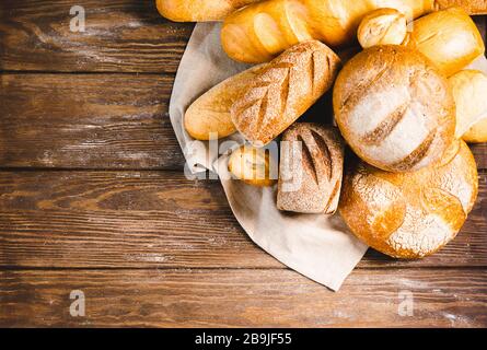 Pane fresco cotto con crosta dorata, pane, focacce, bianco, segale su fondo rustico di legno con sil rustico. Layout piatto Foto Stock