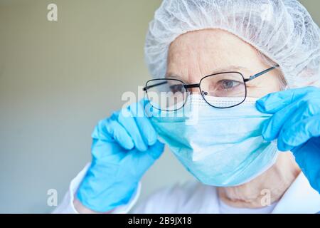 Il vecchio medico in indumenti protettivi mette la protezione della bocca nell'unità di terapia intensiva di una clinica Foto Stock