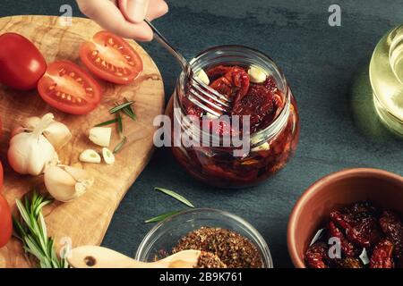 La mano femminile mette i pomodori a forcella in un vaso di vetro con una forchetta. Cottura di pomodori a base di spezie in scatola. Foto Stock
