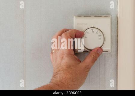 Mano maschio che regola un termostato centrale della stanza di riscaldamento. Foto Stock
