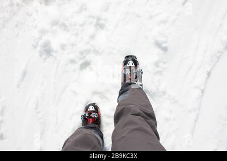 Le gambe dello sciatore con pantaloni neri e i suoi scarponi da sci rossi camminano sulla neve. Concetto di sport invernale Foto Stock