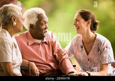 Una coppia senior parla con un'infermiera sorridente mentre si siedono all'esterno. Foto Stock