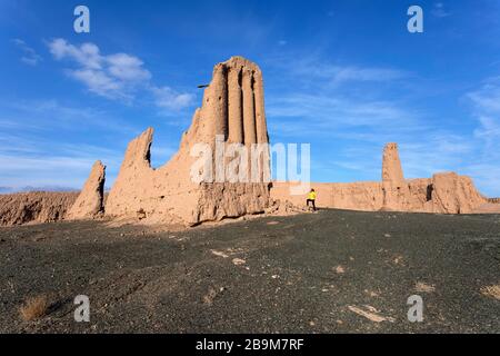 Donna in giacca gialla in piedi alle rovine mozzafiato della fortezza di Jampik Kala situato nel deserto di Kyzylkum nella regione di Karakalpakstan in Uzbekistan Foto Stock