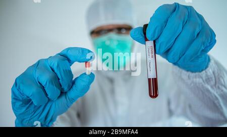 Medico in laboratorio che tiene una pillola e una provetta per l'analisi del sangue su sfondo bianco. Covid-19 sta attualmente cercando di trovare un farmaco contro il virus per trattare Th Foto Stock