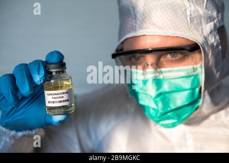 Un medico caucasico in laboratorio, in possesso di vaccini liquidi per le malattie da coronavirus. Maschile scientifico su tuta protettiva con un vaccino Covid-19. Medico Foto Stock