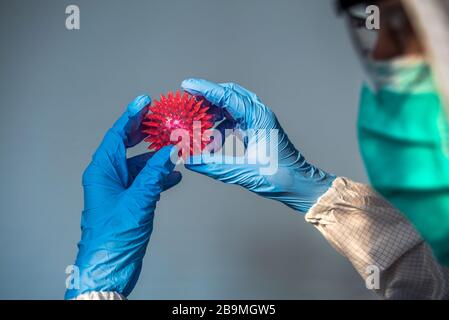 Mani di medico con il modello del virus Corona. Maschile scientifico su tuta protettiva che tiene un Coronavirus. Uomo caucasico con molecola di covid-19. AB Foto Stock