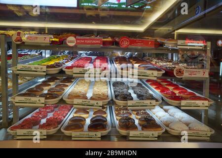 Varietà di ciambelle deliziose in vetrina presso il panificio Krispy Kreme. Vari tipi di ciambelle sul ripiano nel negozio di prodotti da forno. Selezione di dolci. Foto Stock