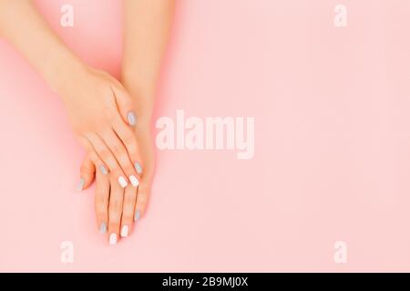 Elegante manicure femminile alla moda. Bella mano di giovane donna con perfetto manicure grigio su sfondo rosa. Stile piatto. Foto Stock