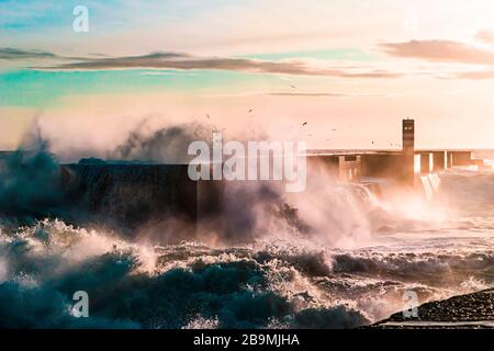 Onde che si schiantano su un molo al tramonto Foto Stock