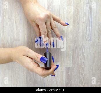 Le mani femminili che fanno il manicure blu di colore di auto lucidano del chiodo su uno sfondo di legno naturale. Foto Stock