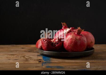 Primo piano di melograni su piatto scuro su tavole rustiche Foto Stock