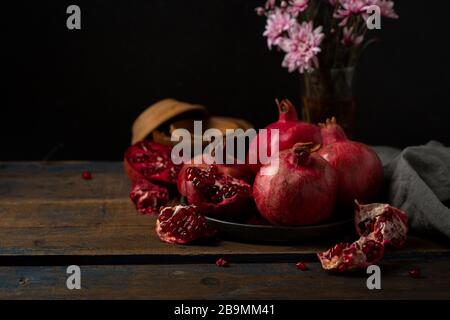 Diversi melograni su piatto su piatto di legno e fiori Foto Stock
