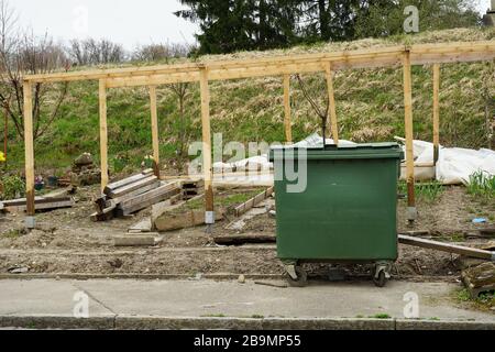 scheletro di legno o cornice di una serra in un giardino di aggiudicazione con un bidone per rifiuti organici in primo piano Foto Stock