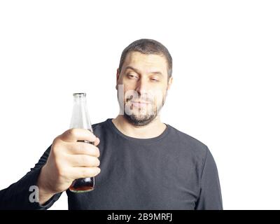 Un uomo dai capelli scuri con barba in abiti neri tiene una bottiglia con una bevanda Foto Stock