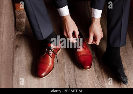 lo sposo ha allacciato i lacci sulle scarpe da lavoro. l'uomo d'affari sta appendendo le scarpe al coperto nella stanza dell'hotel. le mani di mans ed il paio di scarpe da uomo di cuoio. riunione di Foto Stock