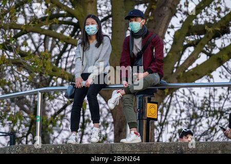 Londra, Regno Unito. 24 marzo 2020. Coronavirus: Una giovane coppia con faccemasks guardare la luce della sera dalla cima del Greenwich Park, mentre PM Boris Johnson annuncia severe misure di blocco esortando le persone a rimanere a casa. Credit: Guy Corbishley/Alamy Live News Foto Stock