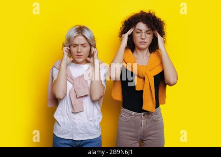 Brunetta caucasiana concentrata con capelli ricci che posa vicino al suo amico biondo mentre pensa su uno sfondo giallo Foto Stock