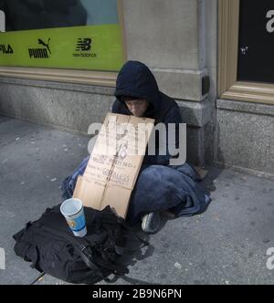 Senzatetto che chiede aiuto per pagare una camera per la notte seduta sulla 5th Avenue nel centro di Manhattan, New York City. Foto Stock