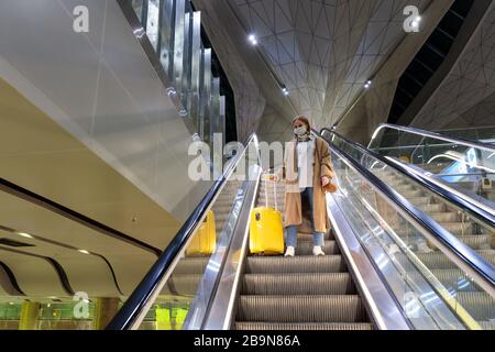 Donna con bagaglio giallo si trova sulla scala mobile presso il terminal dell'aeroporto quasi vuoto a causa delle restrizioni di viaggio per l'epidemia di coronavirus pandemico/Covid-19. Flig Foto Stock