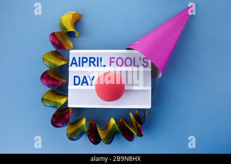 Cappellino da festa e scatola luminosa con frase aprile giorno dello sciocco su campo blu Foto Stock