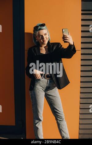 Donna caucasica sicura con capelli blu facendo un selfie fuori di fronte al sole Foto Stock