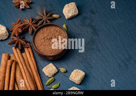 Anice stella marrone e cannella su sfondo scuro. Macinare la cannella in una tazza. Cardamomo e zucchero di canna. Foto Stock