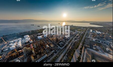 Vista aerea della pianta chimica al tramonto, raffinazione del petrolio, fumo, tubi, inquinamento ecologico, infezione dell'aria, costa del mare in Grecia, petroliere si aspettano Foto Stock