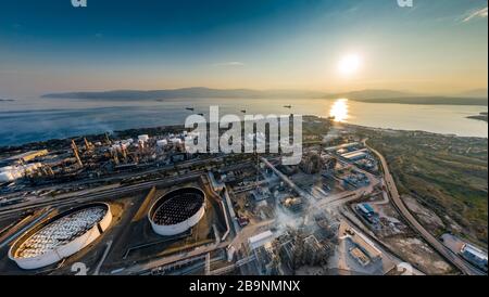 Vista aerea della pianta chimica al tramonto, raffinazione del petrolio, fumo, tubi, inquinamento ecologico, infezione dell'aria, costa del mare in Grecia, petroliere si aspettano Foto Stock